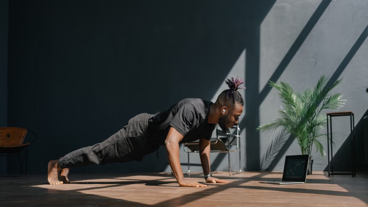 An adult man doing push-ups indoors, guided by a laptop. Fitness and technology merge.
